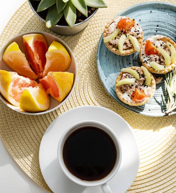 Coffee cup, tartlets and slices of grapefruits, breakfast in morning sunlight.